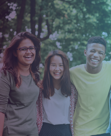 Three diverse students embracing, smiling and laughing into the camera