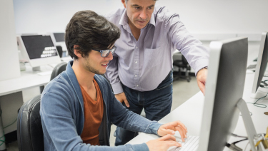 Male adult helping male student on computer