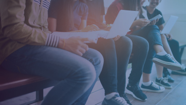 Students sitting on bench with papers and laptops